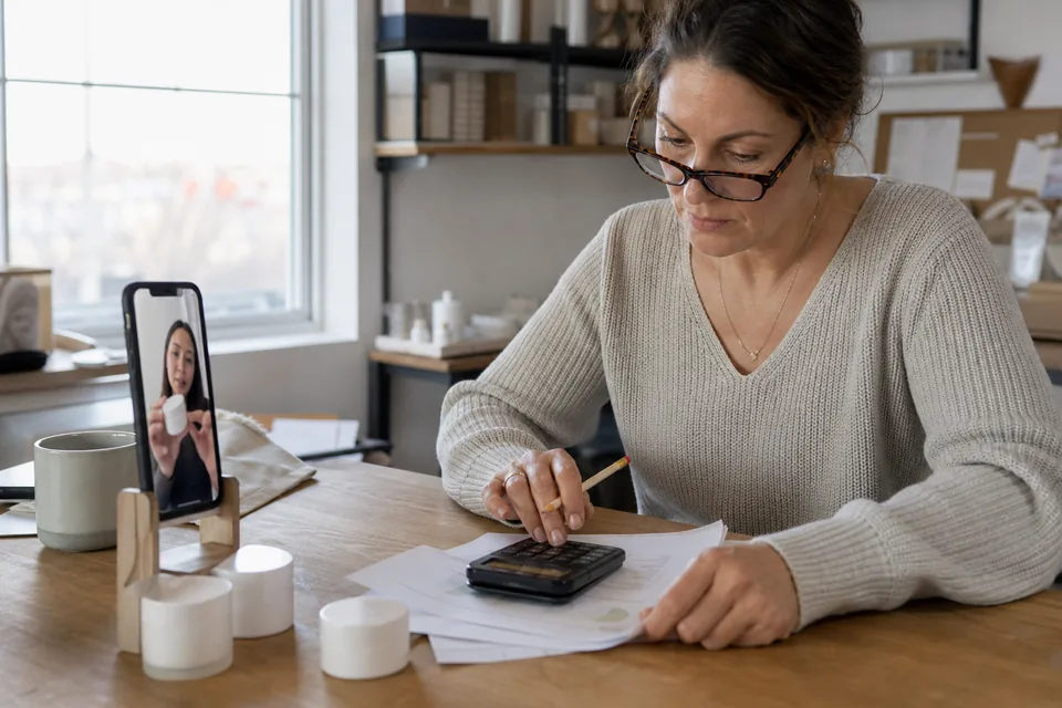 Marketing lead at a small brand comparing a prepaid video budget against creator payouts on a printed sheet with a calculator
