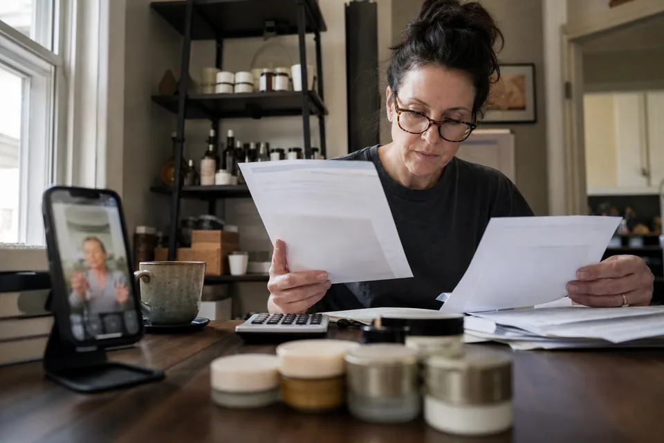 Brand founder adding up a quarterly software invoice against creator payments with a calculator at a kitchen table