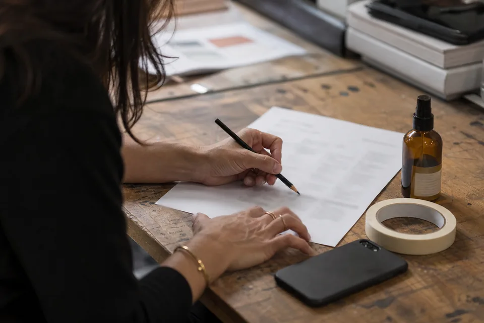 Hands of a brand founder marking up a printed brief next to a product sample and a phone on a small workbench