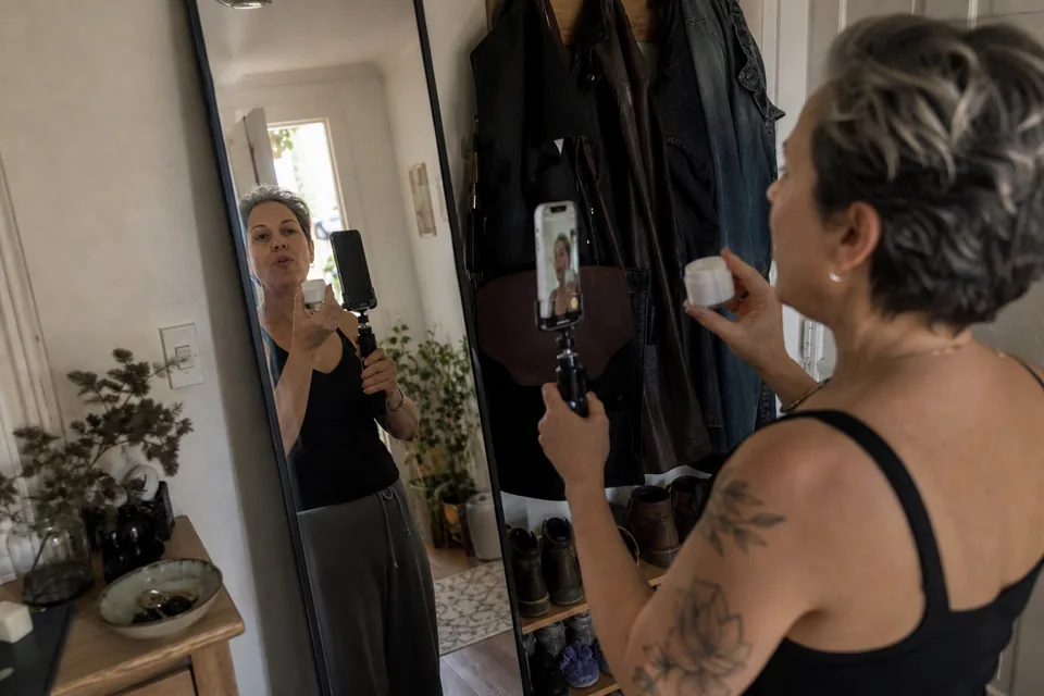 Adult creator recording a short pitch video of herself in a hallway mirror holding a skincare jar