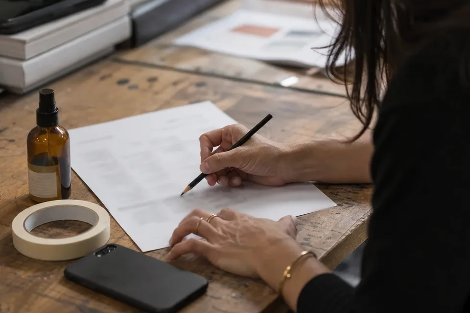 Adult creator reviewing her short video portfolio on a phone at a desk with a tripod beside her